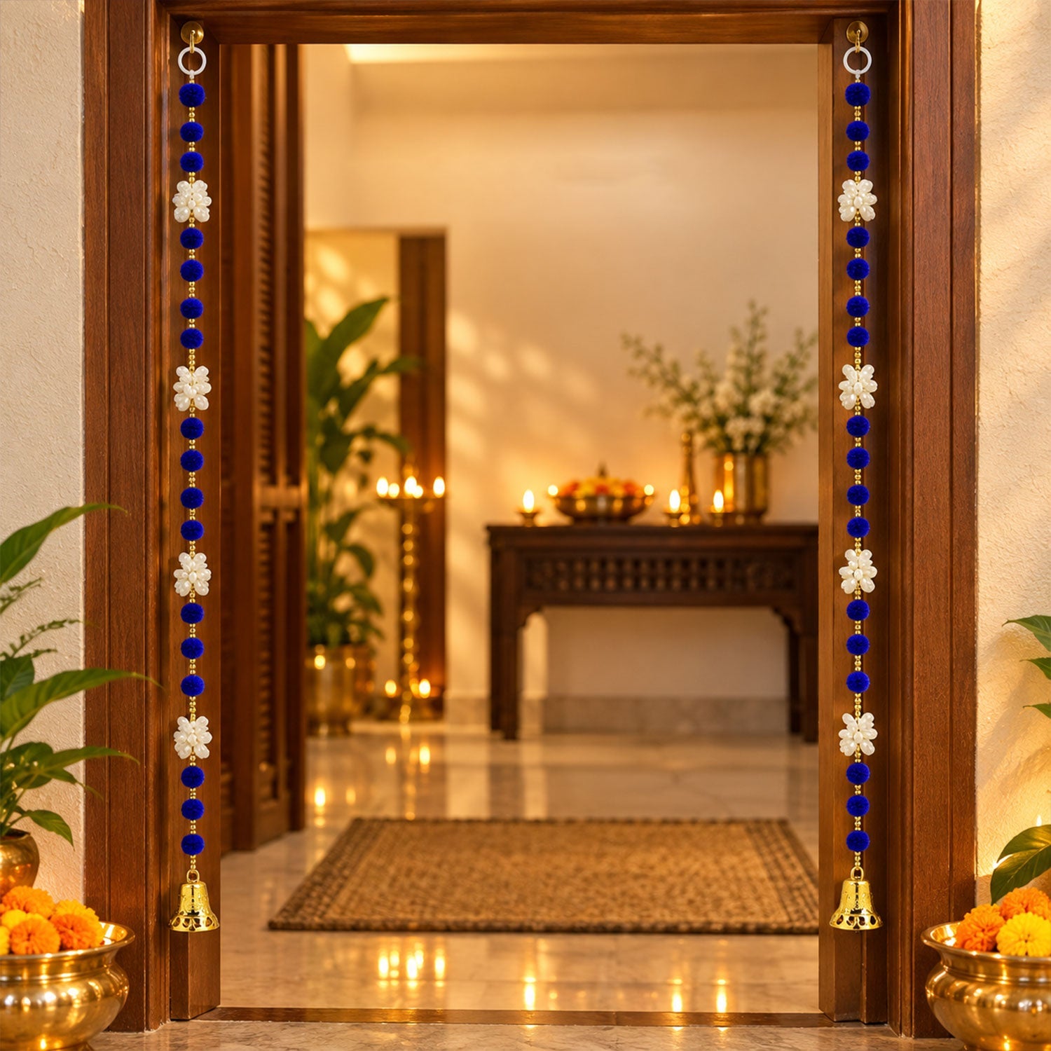 A pair of blue and white decorative hangings with golden bells frame a doorway, with brass pots containing marigolds on the