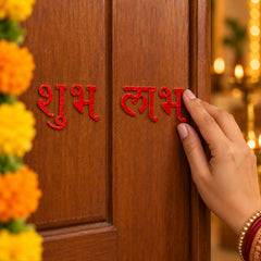 A hand carefully positions a red glitter Shubh sticker onto a polished brown wooden door.