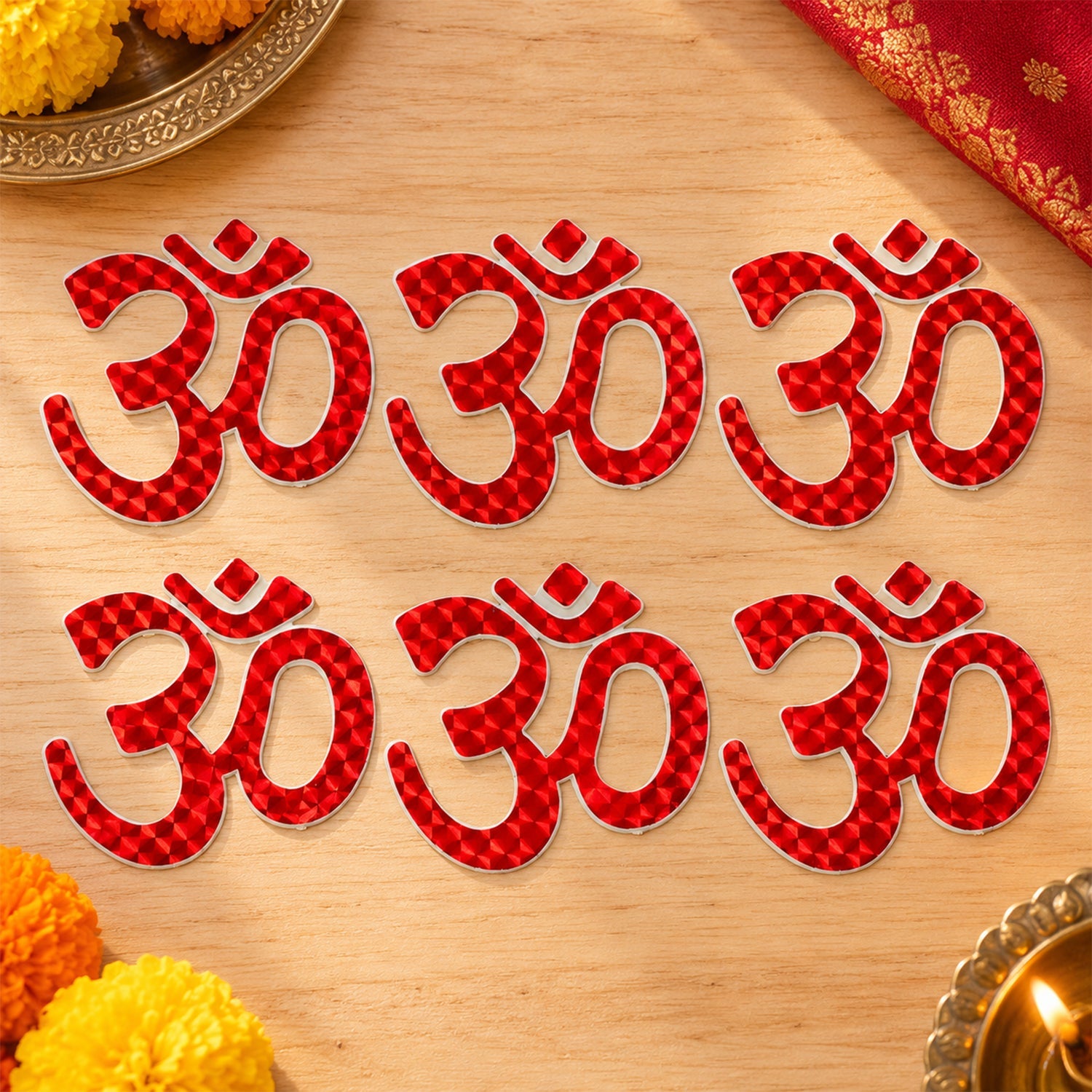 Six red Om symbol stickers are arranged in two rows on a light wooden surface, surrounded by marigold petals.