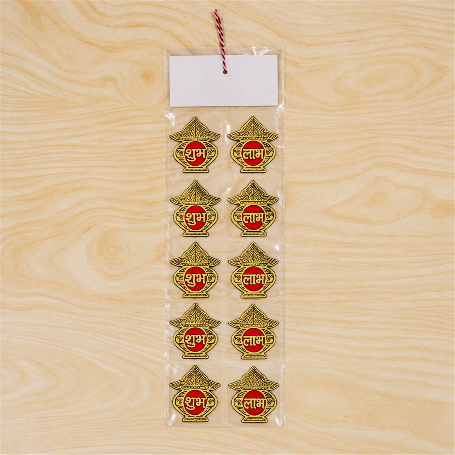 Ten golden Shubh Labh stickers are sealed in clear plastic packaging with a white label on a light wood surface.