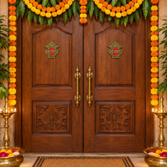 Two golden Shubh Labh stickers adorn a large wooden double door decorated with marigold garlands.