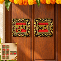Two ornate red and gold Shubh Labh stickers adhere to a wooden door, surrounded by marigold garlands.