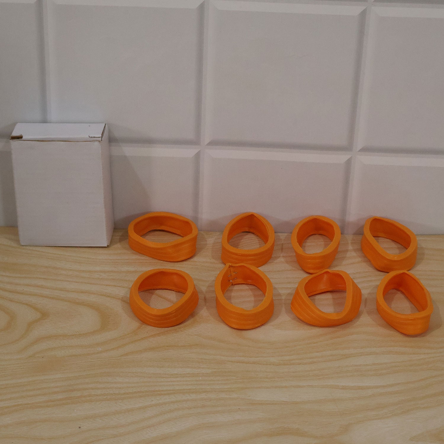 Eight orange silicone wheel covers are scattered on a wooden surface next to a plain white box.