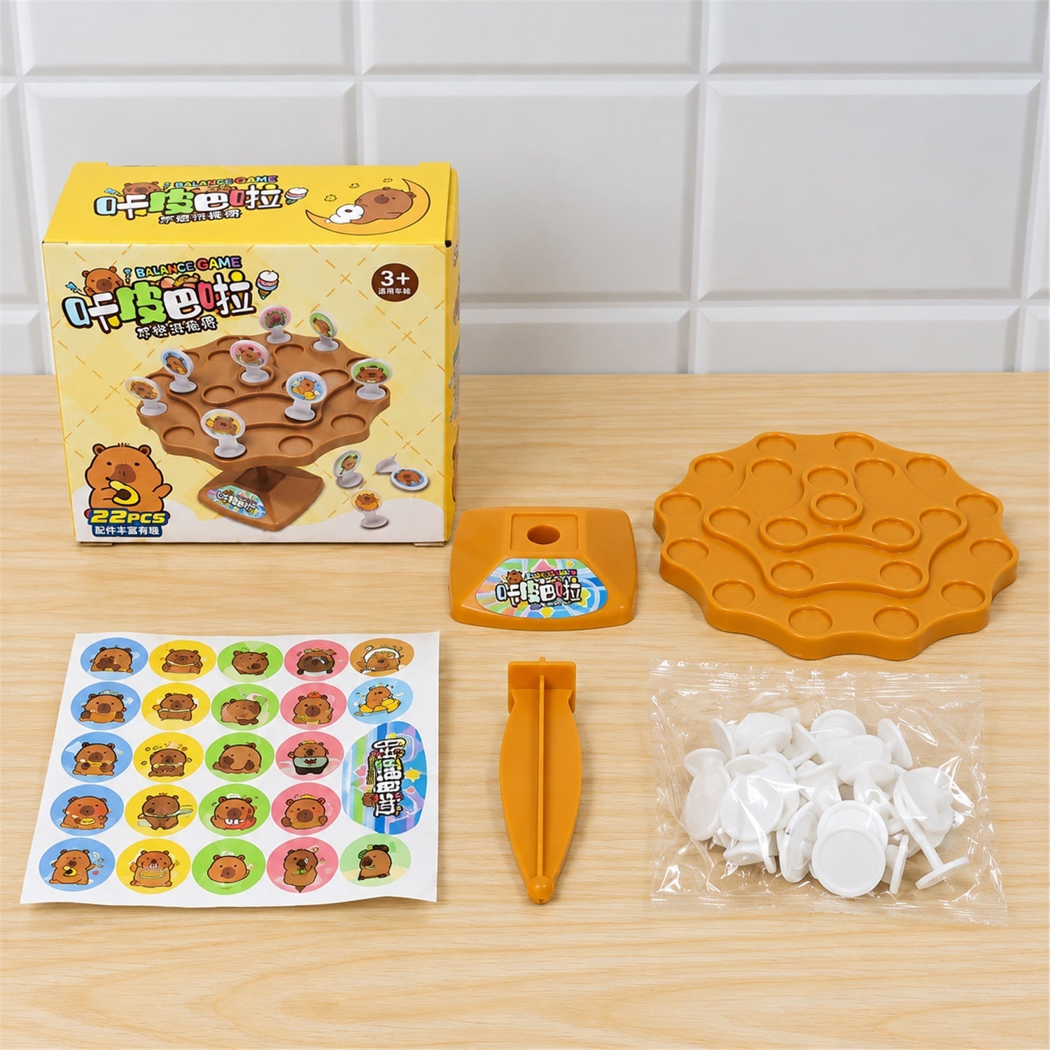 All components of the capybara balance game laid out: box, board, base, stand, sticker sheet, and tokens.