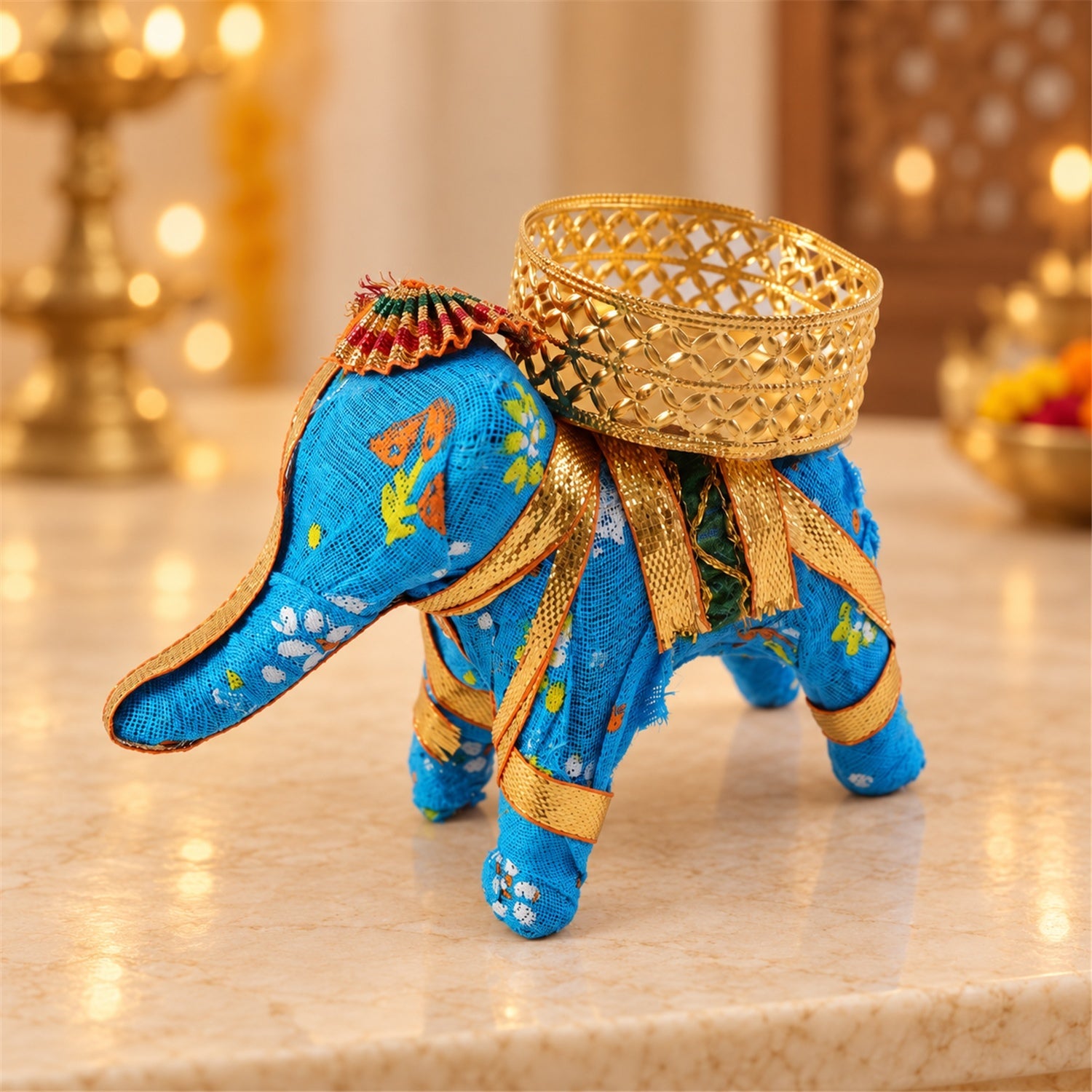 A blue fabric elephant candle holder with a gold lattice cup, viewed from a slightly elevated angle.