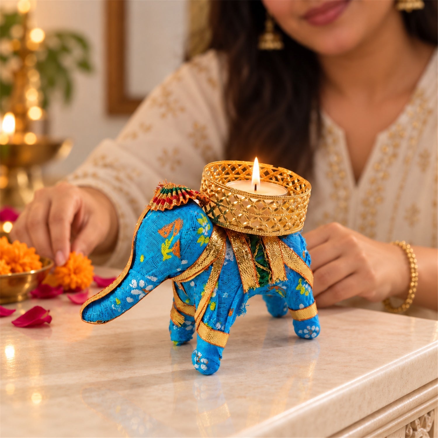 A blue fabric elephant candle holder with a lit tealight sits on a table, a person's hands nearby.