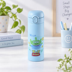 A light blue water bottle with a cartoon alien design stands on a desk beside books and a pen holder.