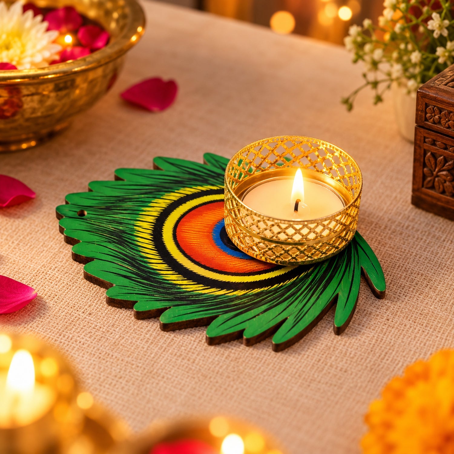 A lit tealight candle in a gold metal holder sits on a green peacock feather shaped base on a light brown surface.