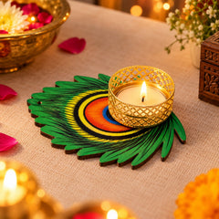 A lit tealight candle in a gold metal holder sits on a green peacock feather shaped base on a light brown surface.
