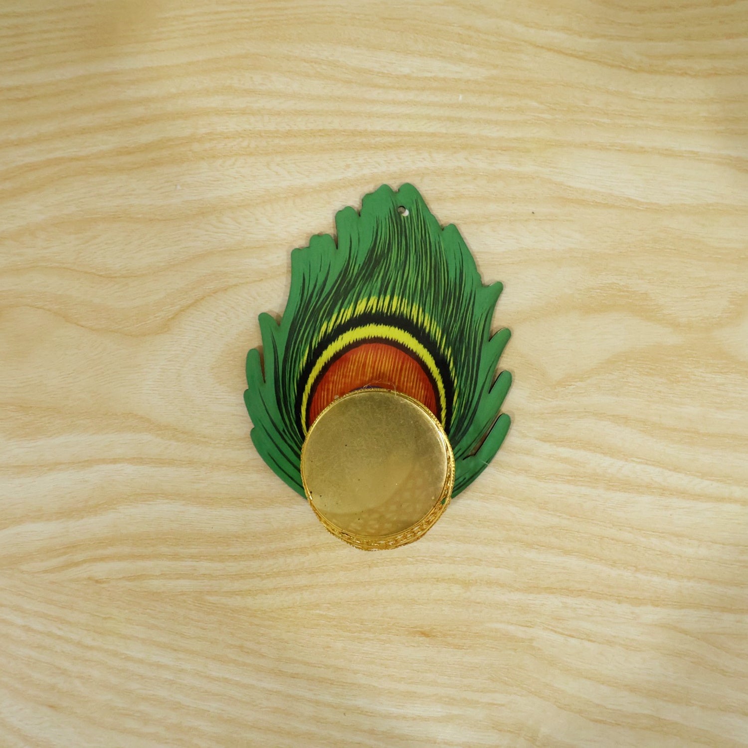 A single peacock feather shaped tealight holder with a gold cup, viewed from above on a wooden surface.