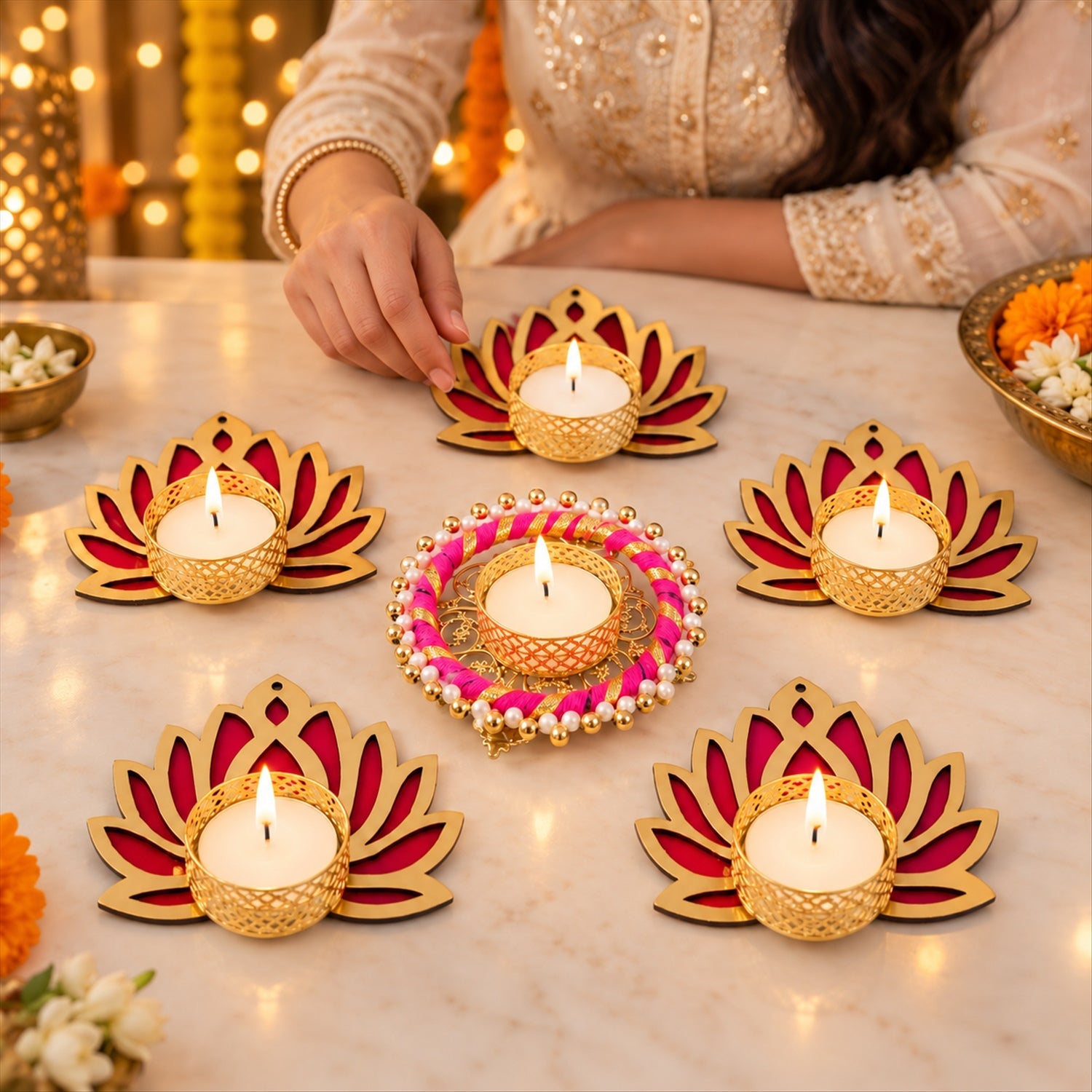 A person's hand lighting a candle in one of the six golden and magenta lotus-shaped tealight holders on a wooden table.