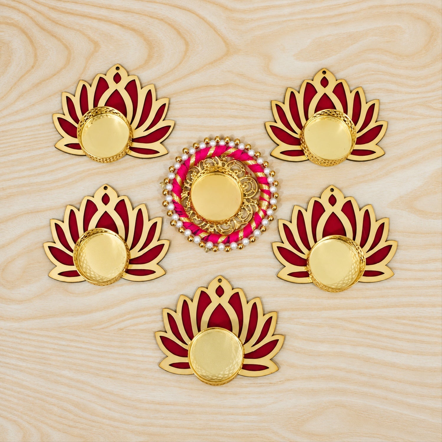 Overhead view of six golden and magenta lotus-shaped tealight holders without candles on a light wooden surface.
