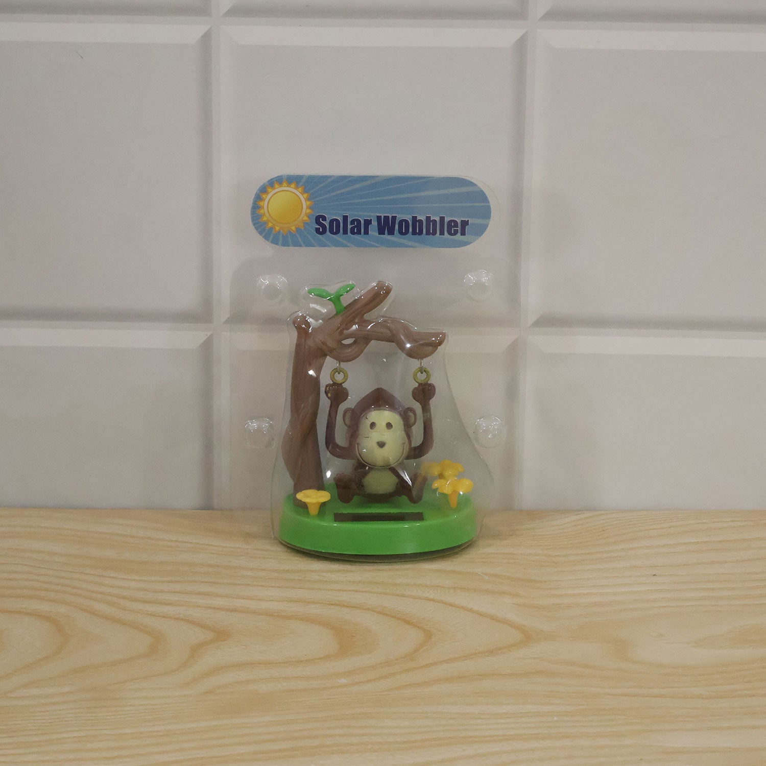 The solar monkey decoration is sealed in clear plastic packaging with a "Solar Wobbler" label, resting on a light wooden