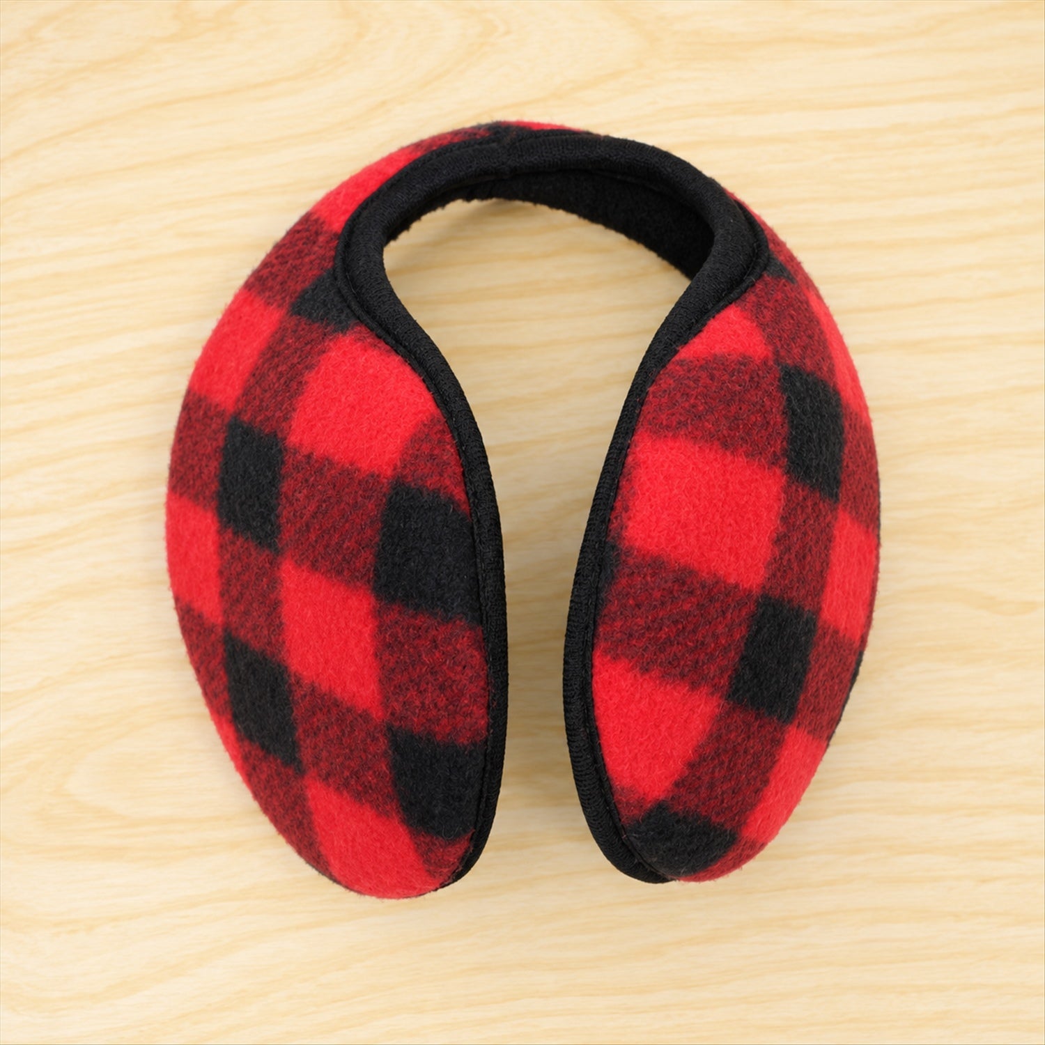 Red and black plaid ear warmers with a black band are positioned on a light wooden background.