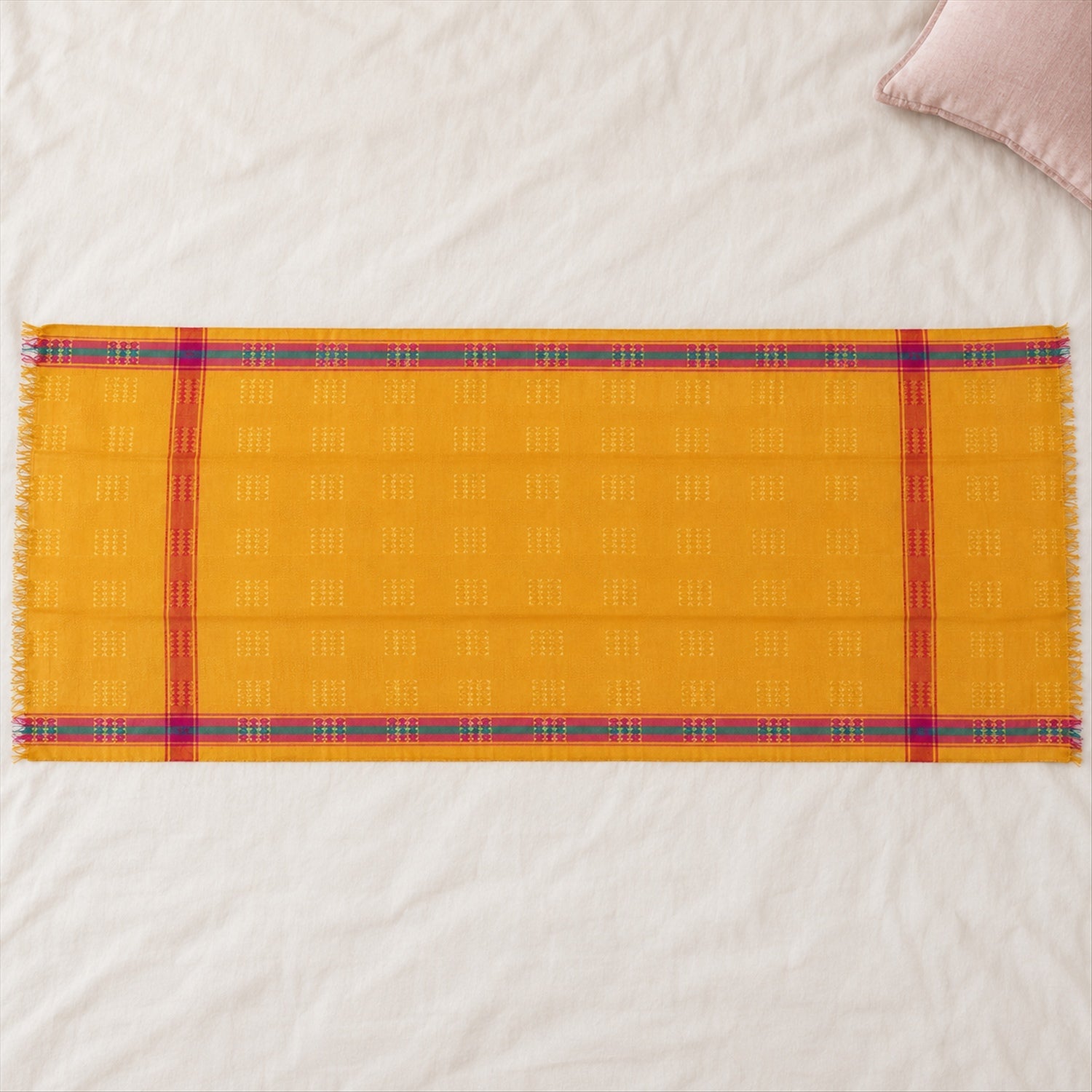 A yellow dupatta with woven square motifs and striped borders in pink and teal is spread on a textured white surface.