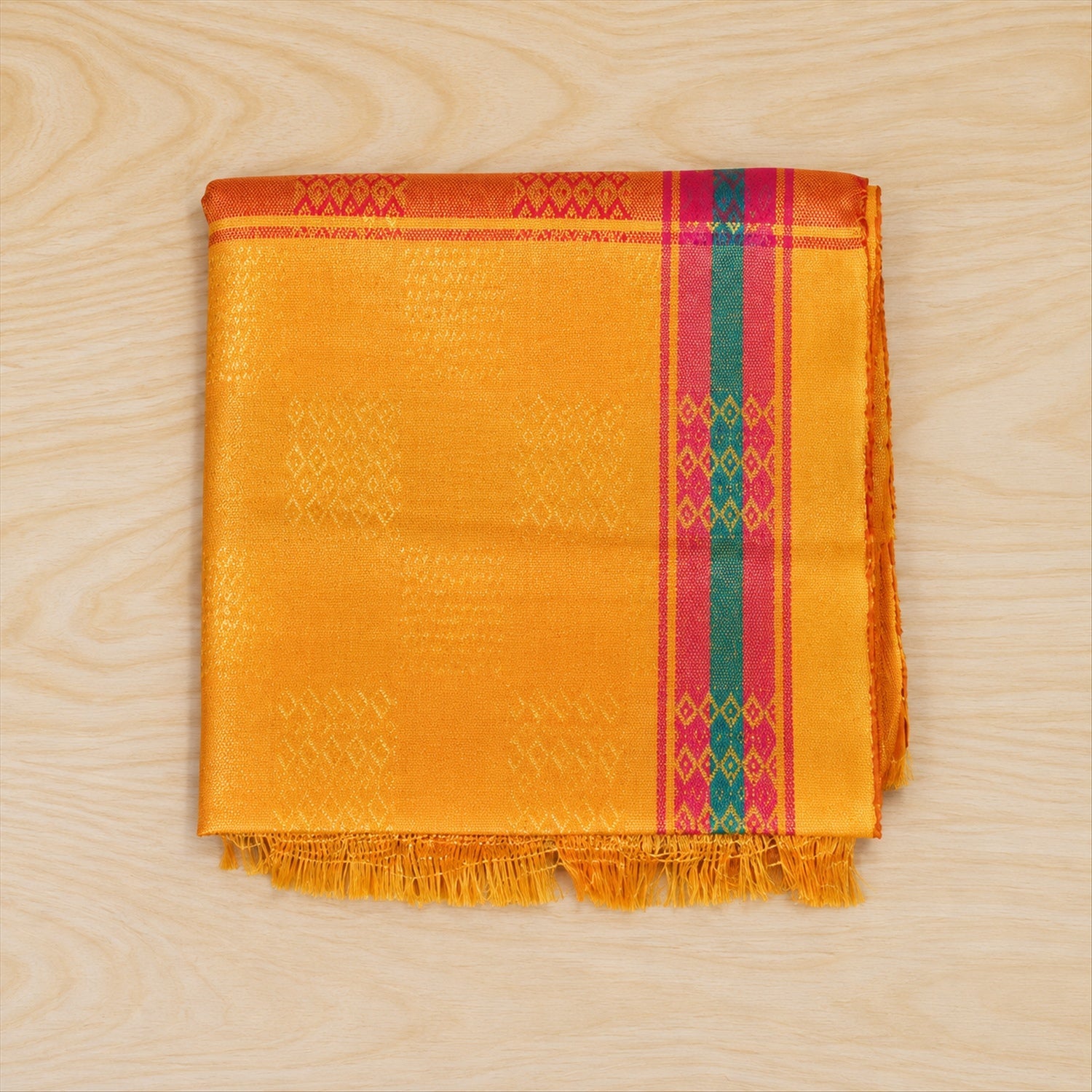 A neatly folded yellow dupatta with intricate woven patterns and vibrant pink and teal striped borders rests on a wooden