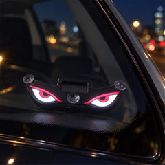Black evil eye light with glowing red and white eyes attached to a car window at night, viewed from inside.