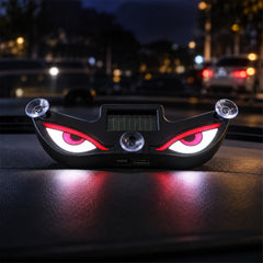 Black evil eye light with red and white glowing eyes, suction cups, and a solar panel on a car dashboard at night.