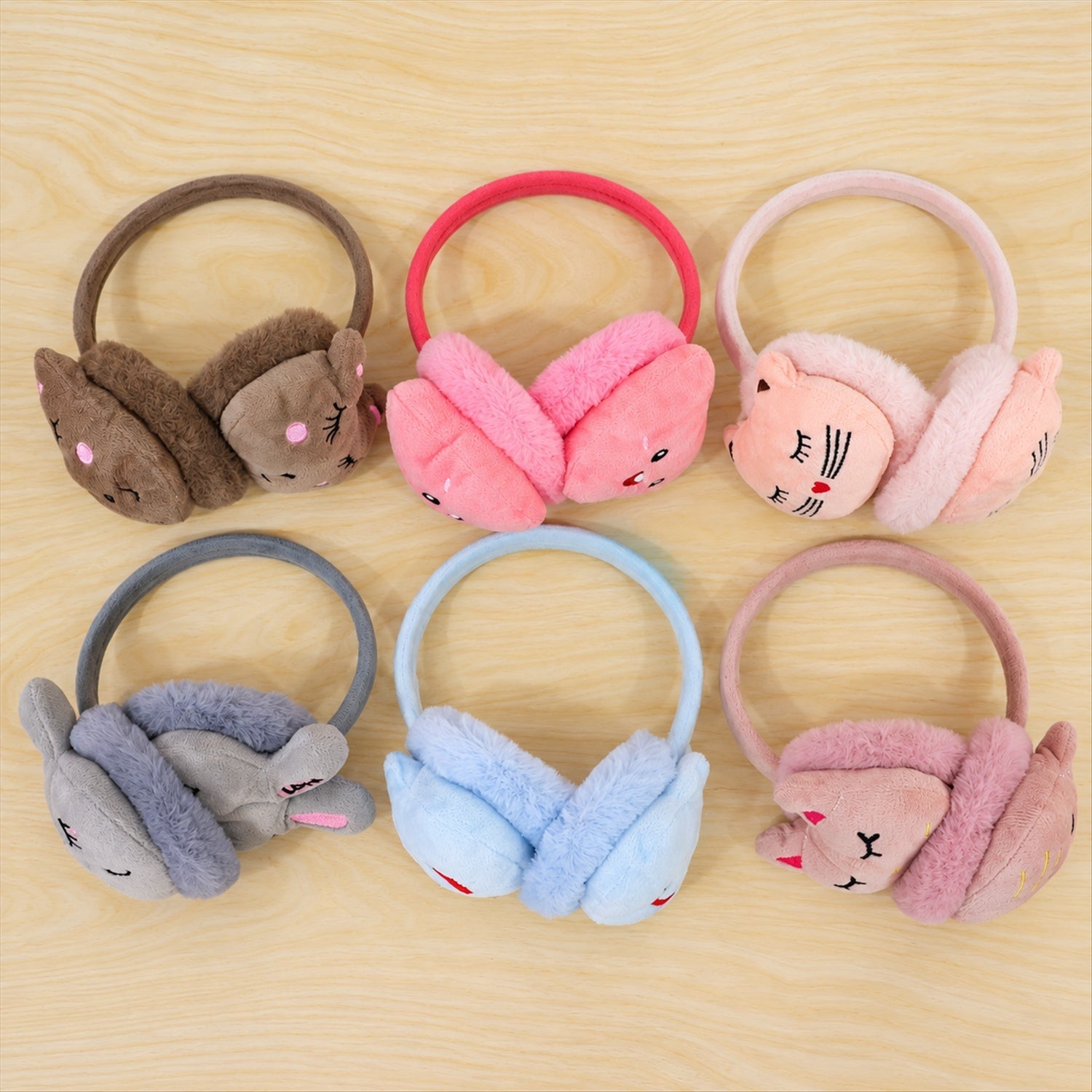 Six pairs of colorful plush earmuffs, each with a different animal face design, are arranged on a wooden surface.