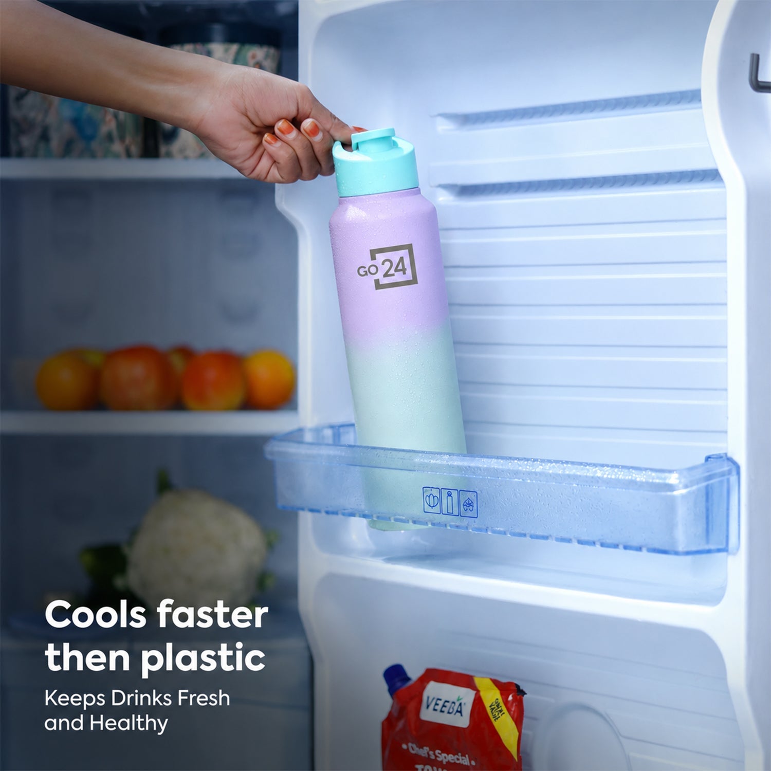 A hand places the purple and mint water bottle into a refrigerator shelf, surrounded by fresh produce.