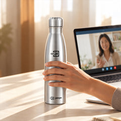 A hand holds a silver water bottle on a desk, with a laptop displaying a video call in the background.