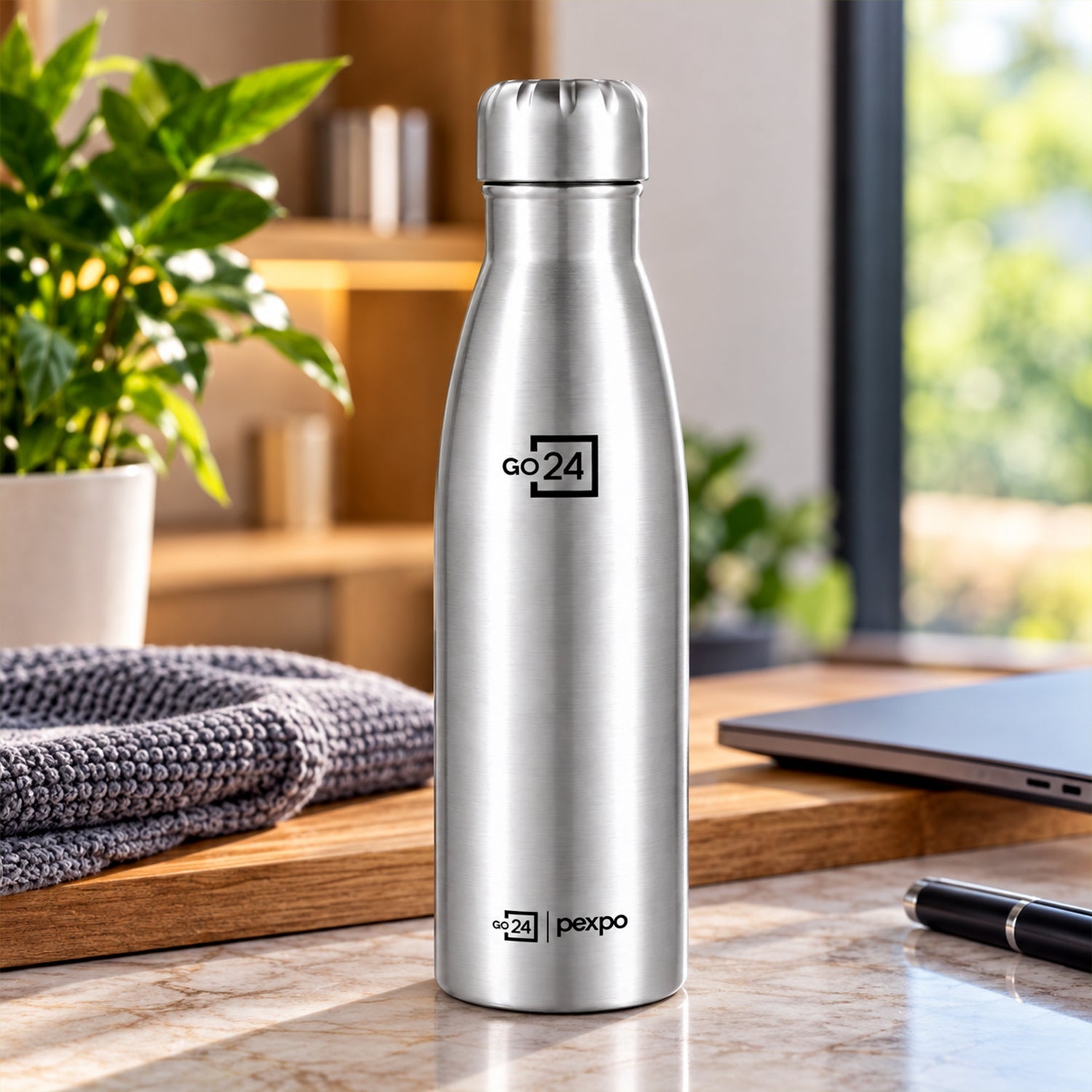 A silver water bottle sits on a wooden surface next to a folded gray towel and a closed laptop.