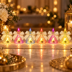 Six LED flameless candles with bows in various colors illuminate a table amidst blurred festive lights.