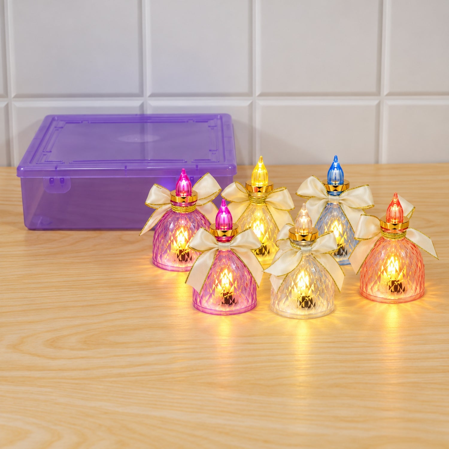 Six colorful LED flameless candles with bows are arranged on a wooden surface next to a purple storage box.