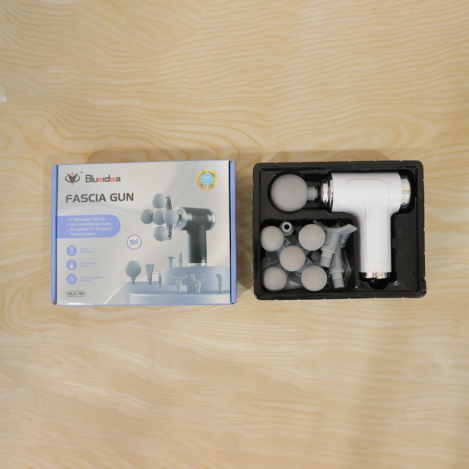 The white fascia massage gun set, including the device and various heads, neatly arranged in its packaging next to the