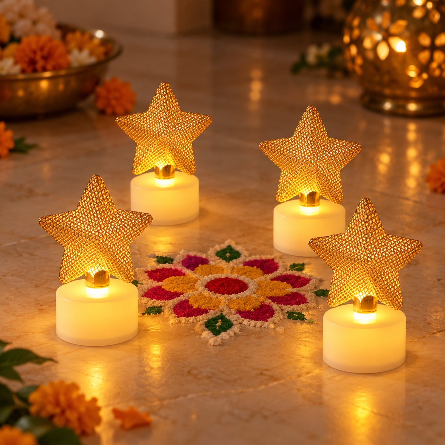 Four golden mesh star LED candles illuminate a colorful rangoli design on a tiled floor, surrounded by marigolds.