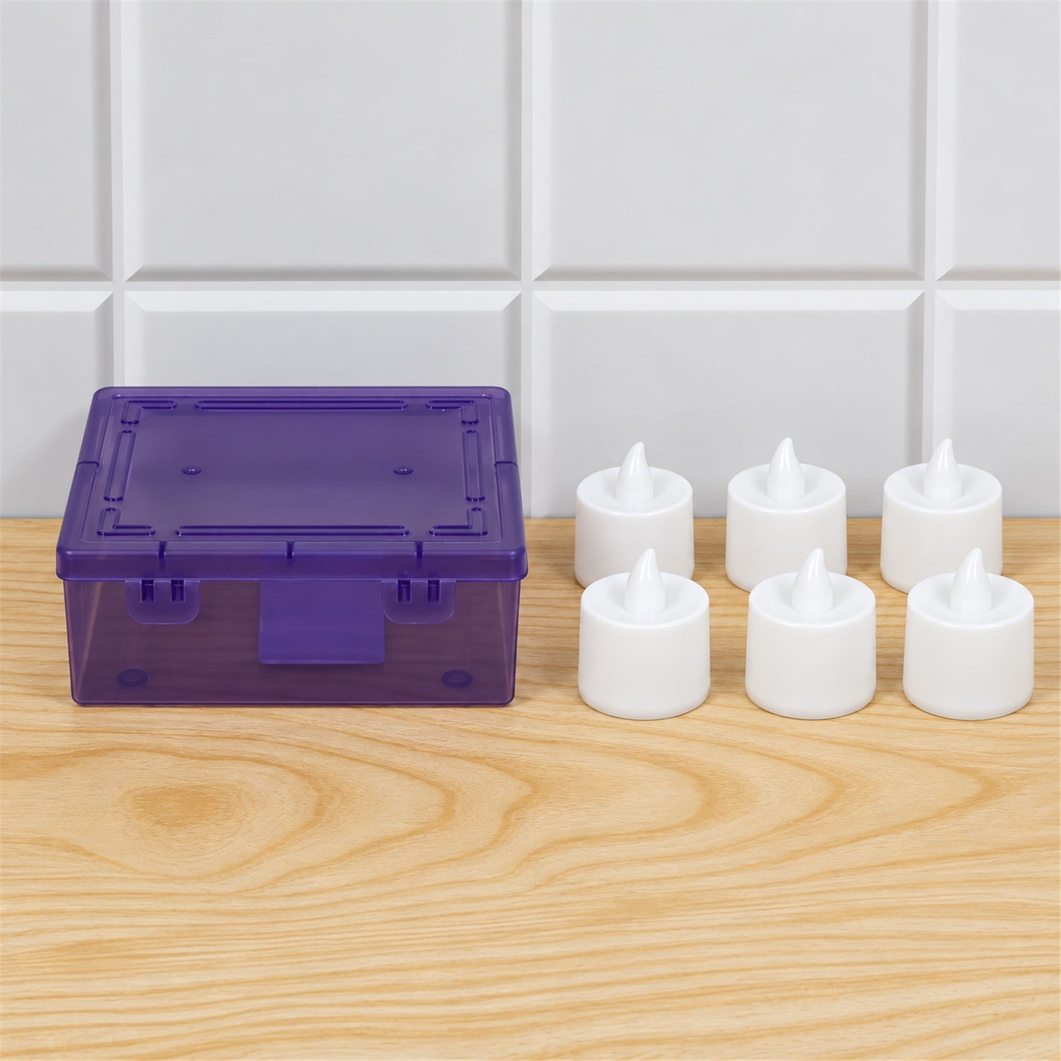Six unlit white flameless LED tealight candles next to a translucent purple storage box on a light wooden surface.