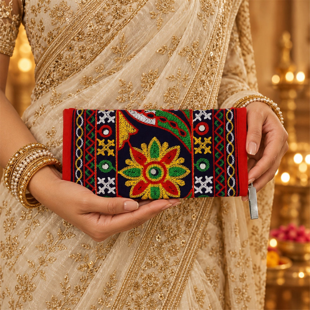 A person in a golden saree holds a dark blue and red embroidered clutch with a colorful floral design.