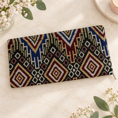 A closed geometric patterned clutch wallet lies on a white marble surface, surrounded by delicate white flowers and green