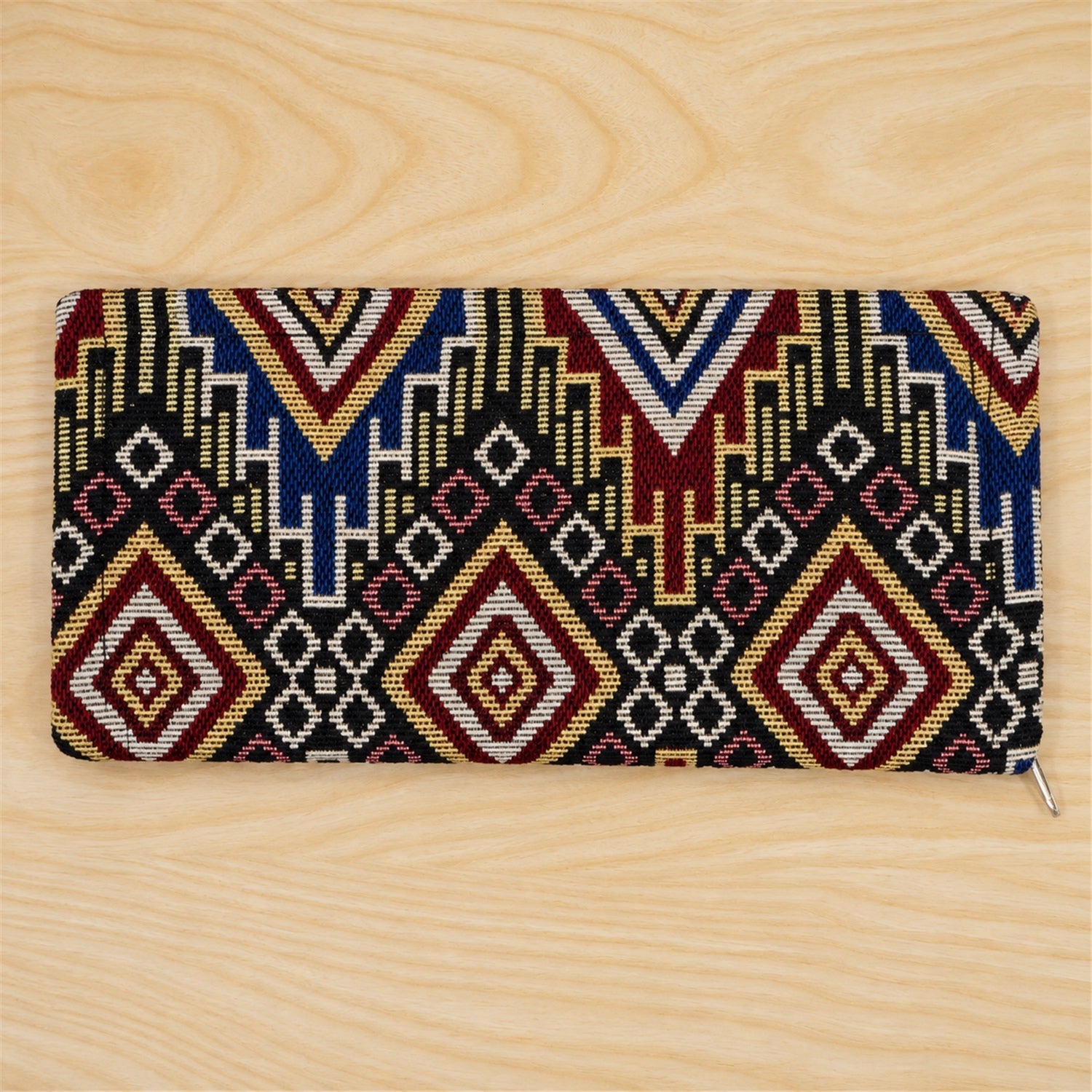 A closed rectangular clutch wallet with a detailed geometric pattern in various colors, resting on a light wooden surface.