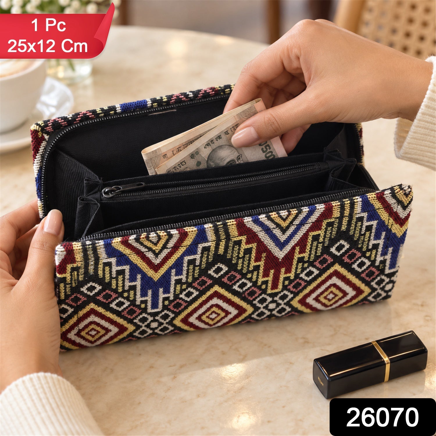 A person's hands insert money into an open, colorful geometric clutch wallet, with a black lipstick tube nearby.