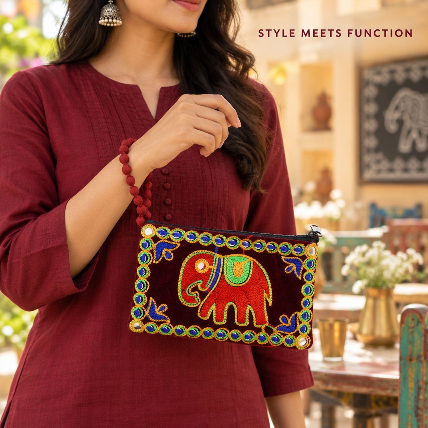 A woman holds a dark red velvet clutch purse with an embroidered elephant and beaded trim, showcasing its style and function.