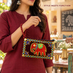 A woman holds a dark red velvet clutch purse with an embroidered elephant and beaded trim, showcasing its style and function.