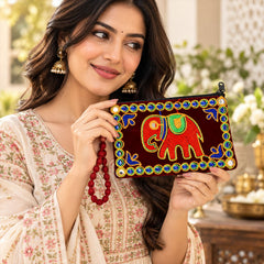 A woman holds a dark red velvet clutch purse with a vibrant red elephant embroidery and blue and green beaded trim.
