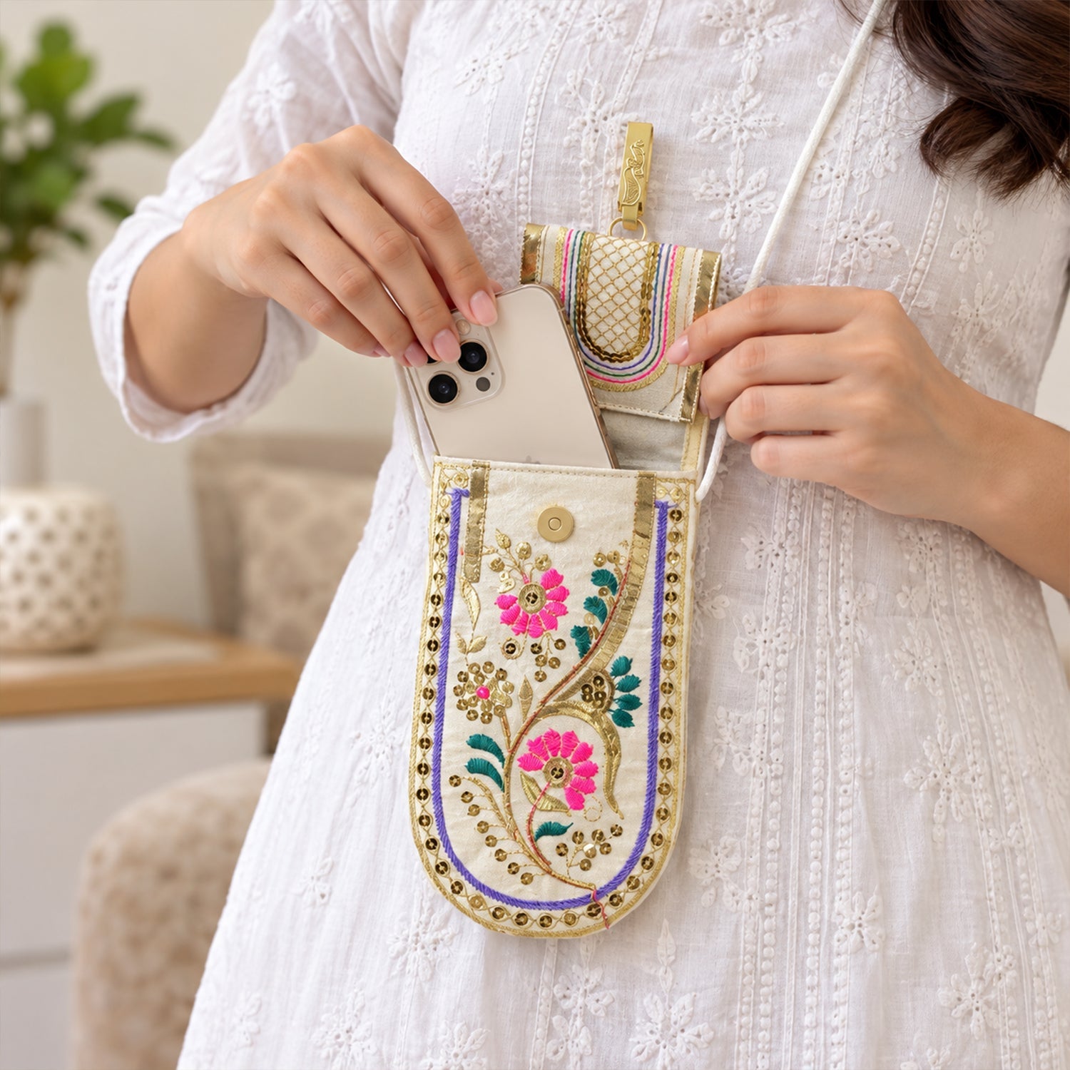 A person in a white dress places a white smartphone into an open embroidered mobile pouch.