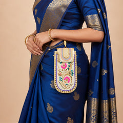 A person wearing a blue sari with gold accents carries an embroidered mobile pouch with a gold chain strap.