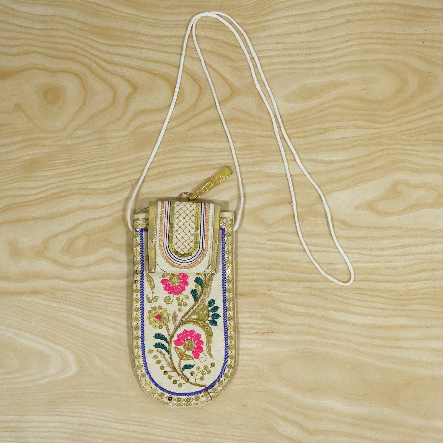 A white embroidered mobile pouch with a white sling strap and gold clip is displayed on a light wooden surface.