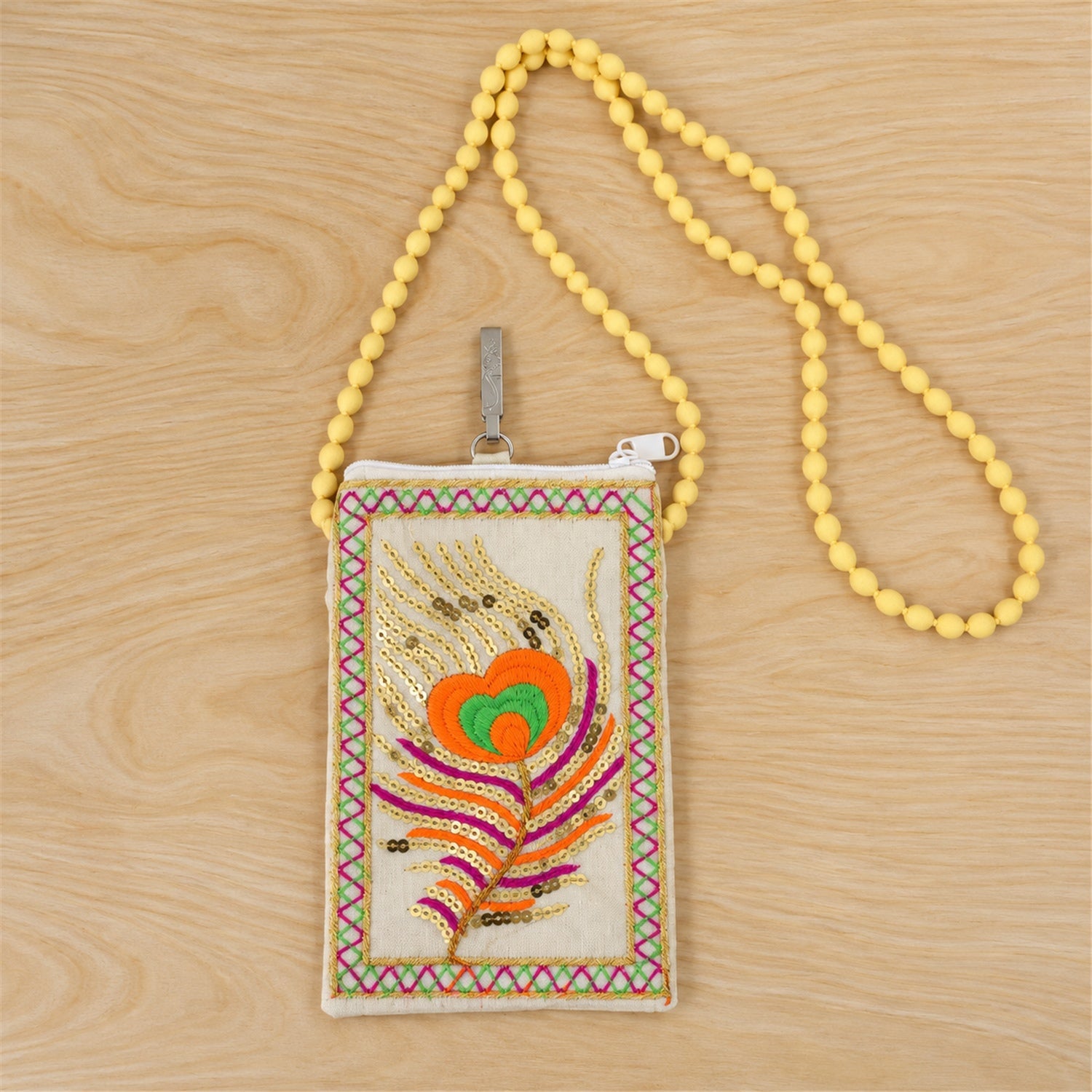 A cream mobile phone pouch with a colourful embroidered peacock feather and a long yellow beaded strap lies on a light