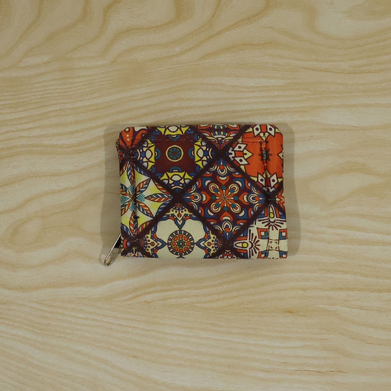 The small, patterned fabric coin purse with a zipper closure is centered on a light wooden surface.