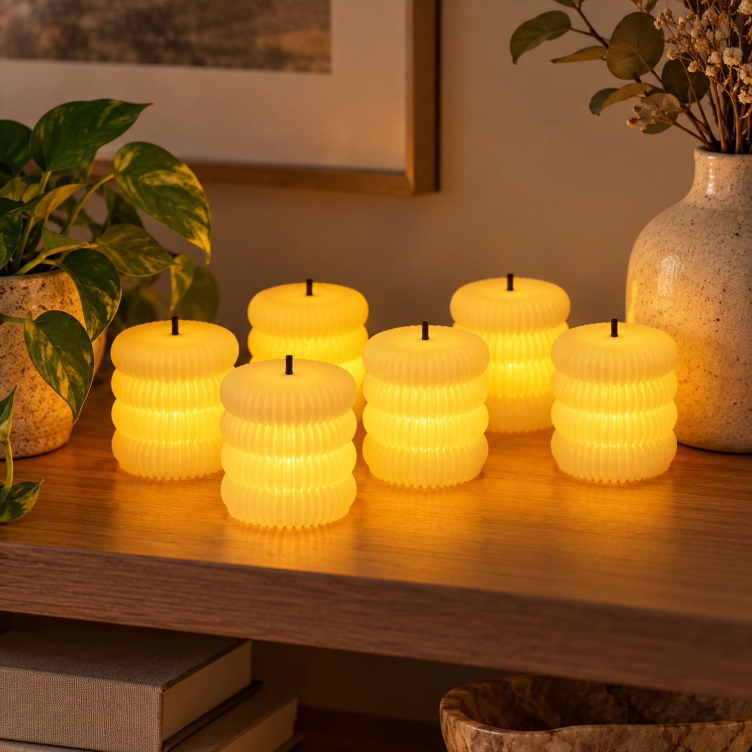 Six glowing ribbed flameless LED tealight candles on a wooden shelf next to potted plants and a vase.