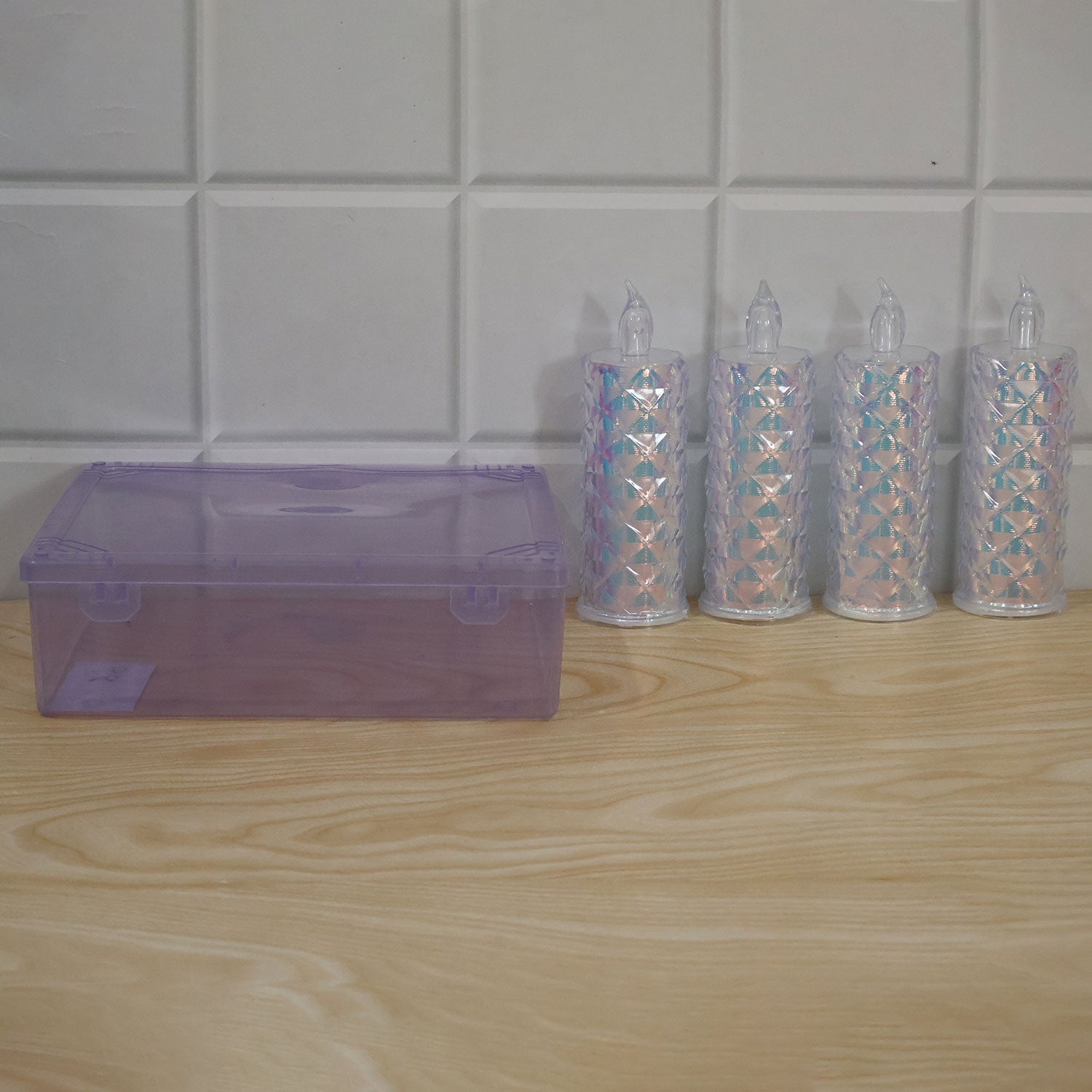 Four unlit crystal LED candles and a closed purple storage box are arranged on a light wooden surface against a white tiled