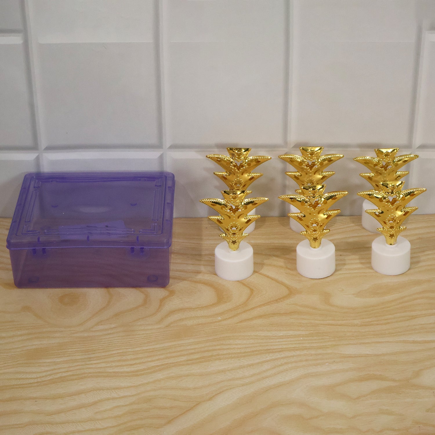 Six golden pineapple LED tealights next to a translucent purple storage box on a wooden surface.