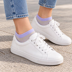 A person's feet wearing light purple and yellow striped ankle socks with white sneakers and blue jeans outdoors.