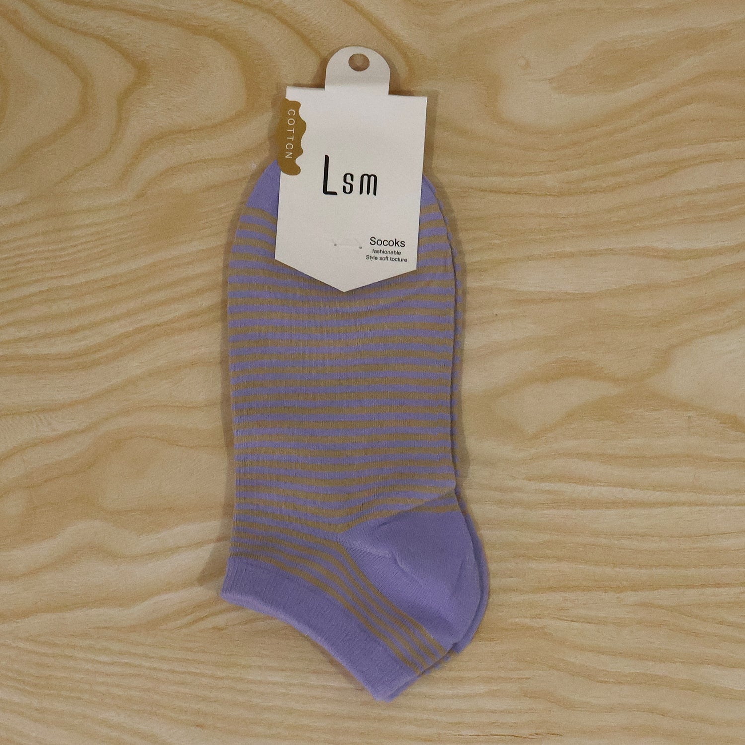 A single light purple and yellow striped ankle sock with a white product tag, lying on a light wooden surface.