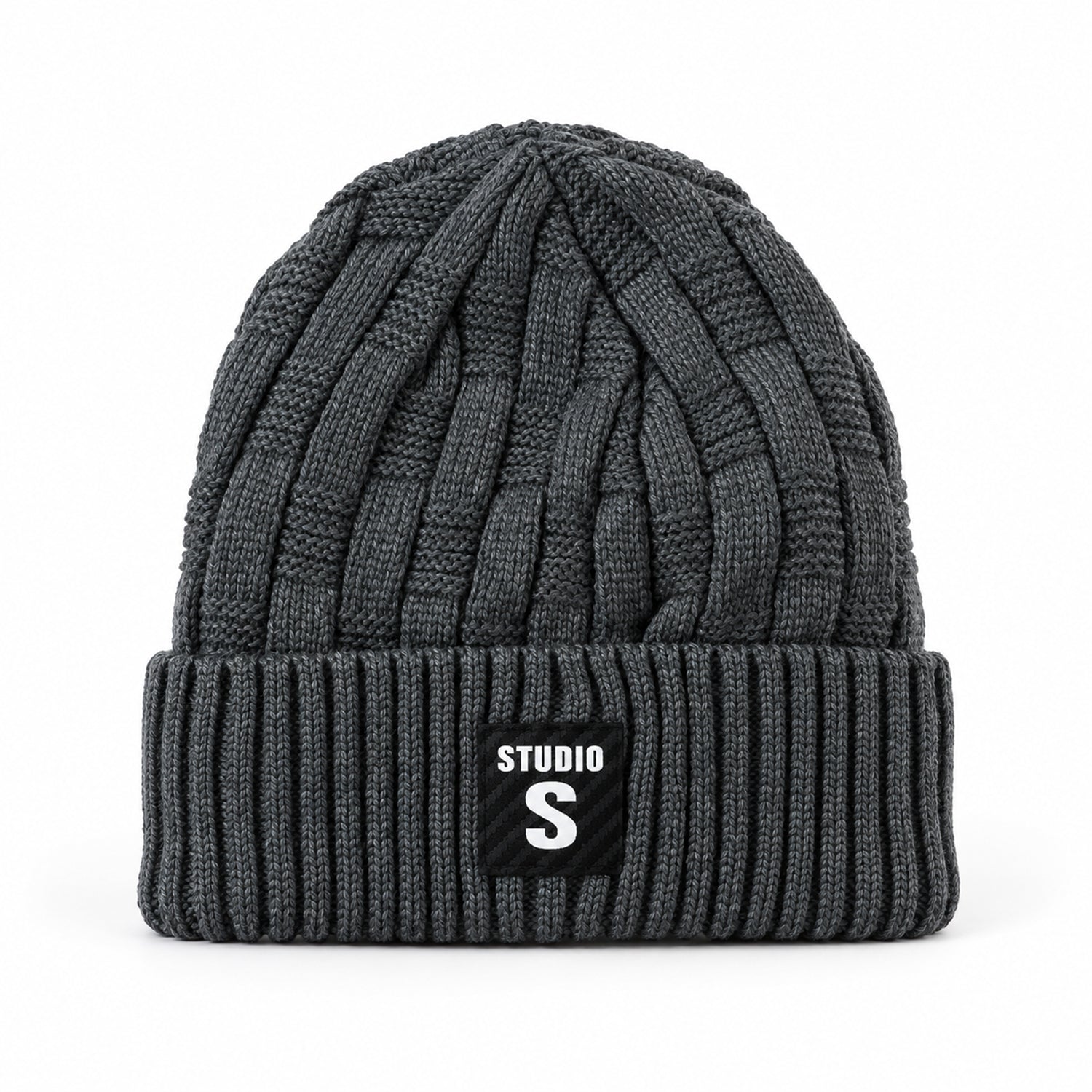 A dark grey cable knit beanie with a ribbed cuff and a black label with "STUDIO S" in white, against a plain white
