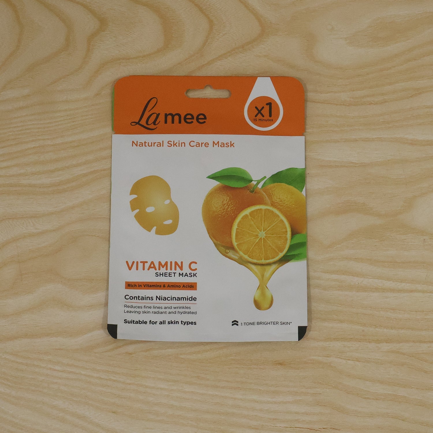 A single white and orange sheet mask package lies flat on a light brown wooden surface.